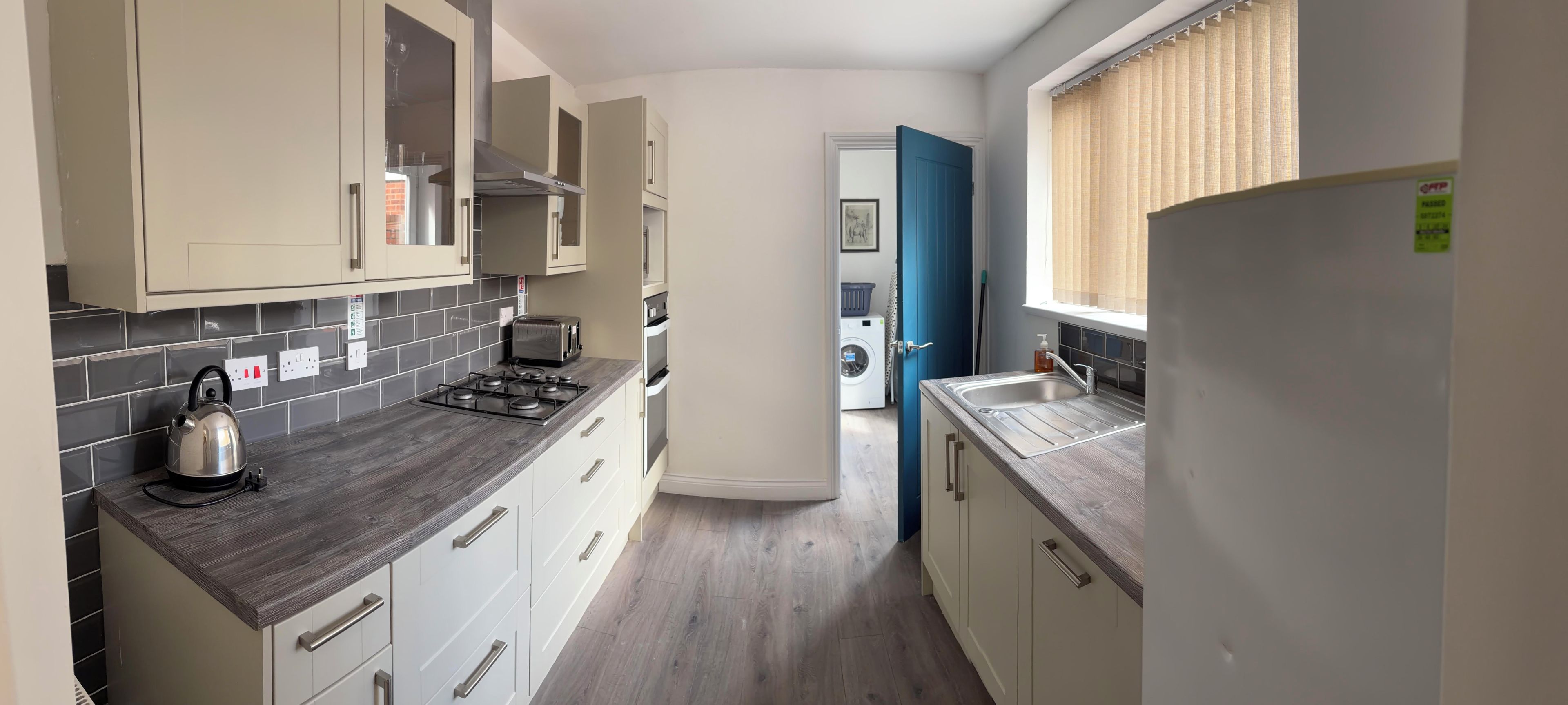 A compact kitchen with a gas stove, a kettle, and a toaster. There is a washing machine and a blue door in the background.
