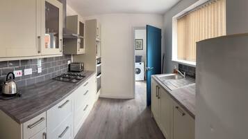 A compact kitchen with a gas stove, a kettle, and a toaster. There is a washing machine and a blue door in the background.