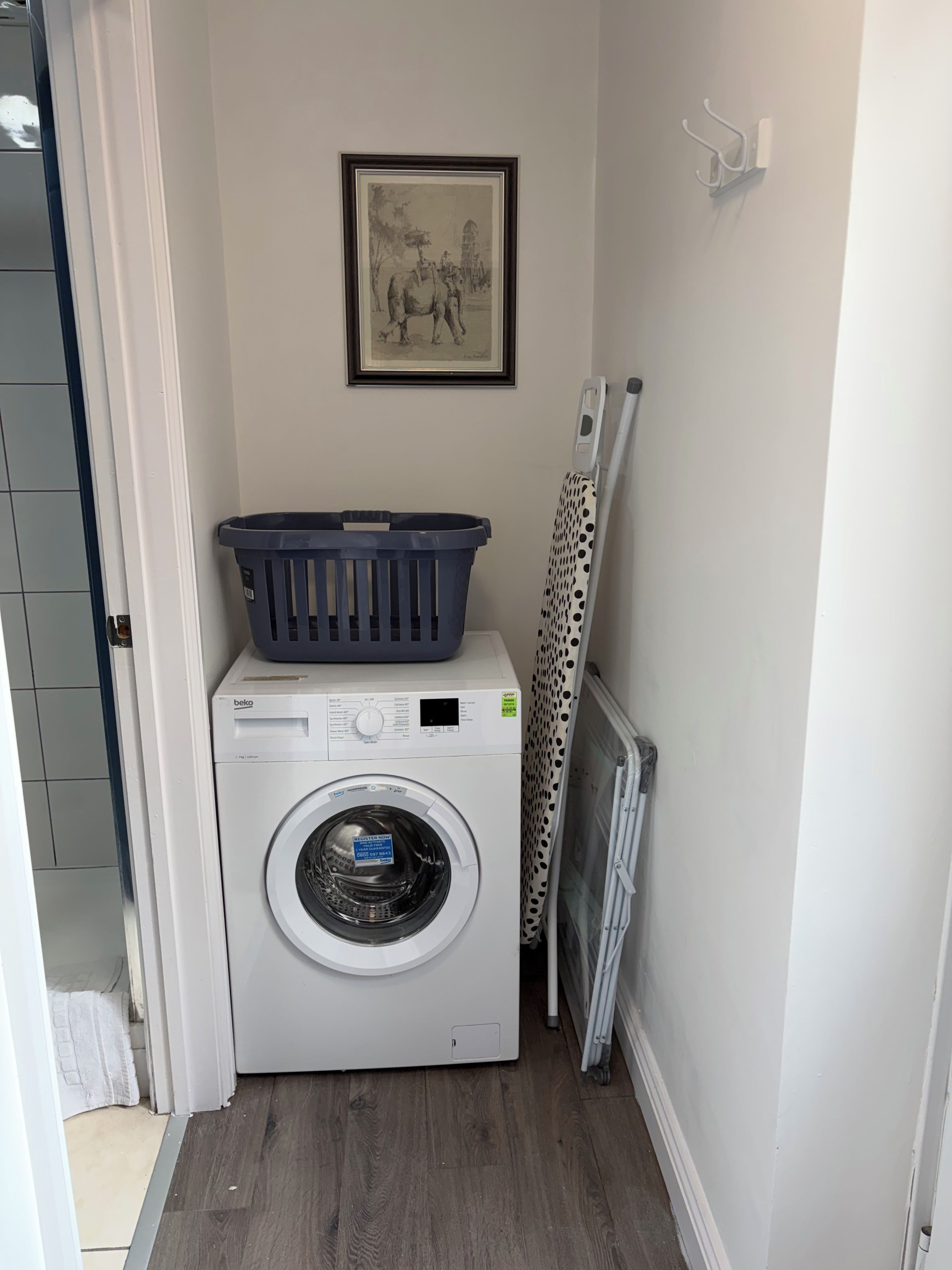 A laundry area with a washing machine, a drying rack, and a framed picture on the wall.