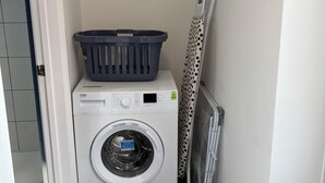 A laundry area with a washing machine, a drying rack, and a framed picture on the wall.