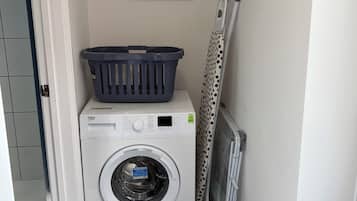 A laundry area with a washing machine, a drying rack, and a framed picture on the wall.