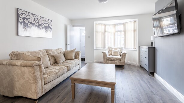 A living room with a sofa, a coffee table, a chair, and a TV mounted on the wall. - Platform Holderness House (Hull)