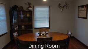 A dining room with a wooden table and chairs, a cabinet with decorative items, and a wall-mounted deer skull.