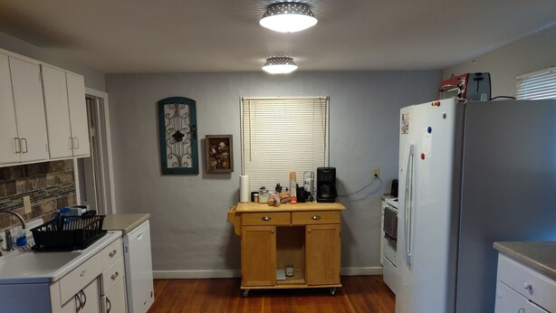 A full kitchen with white cabinets, a wooden countertop, a refrigerator, and a window with blinds.