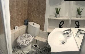 Kylpyhuone, jossa on wc, bidee, pesuallas ja kaksi ruukkukasvia hyllyillä.