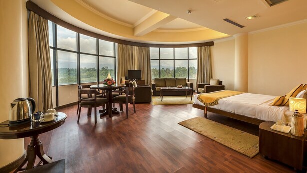 A spacious hotel room with a curved ceiling, large windows offering a scenic view, a cozy seating area, and a neatly made bed. - Summit Residency Airport Hotel (Kathmandu)