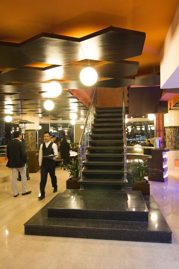 A modern hotel lobby with a central staircase, a reception desk, and a seating area.