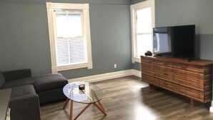 A living room with a sectional sofa, a glass coffee table, a wooden entertainment center, and a flat-screen TV. - Lovely 4 bedroom Home with a patio (Oakland)