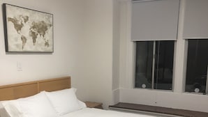 A neatly made bed with white linens, a wooden headboard, a small bedside table, and a world map artwork on the wall. - Lovely 4 bedroom Home with a patio (Oakland)