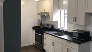 A kitchen with white cabinets, a black countertop, a stove, a sink, and a microwave. - Lovely 4 bedroom Home with a patio (Oakland)