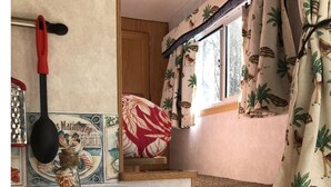Un intérieur chaleureux avec une table où est posé un menu, un vase décoratif et une fenêtre ornée de rideaux aux motifs tropicaux.