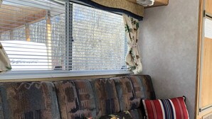 Un intérieur de camping-car chaleureux, avec un canapé à motifs, des meubles en bois et une fenêtre équipée de stores.