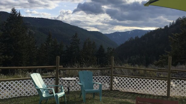 Une terrasse avec deux fauteuils Adirondack verts, un banc en bois et une clôture en treillis blanche.
