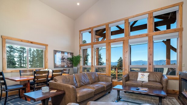 A spacious living room with a large window, a fireplace, and a cozy seating area. - 4 king beds w/ ensuites | Double the Living Space! (Bigfork)