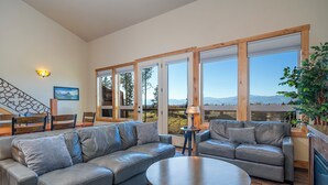 A spacious living room with two leather sofas, a round coffee table, and large windows offering a mountain view. - 4 king beds w/ ensuites | Double the Living Space! (Bigfork)