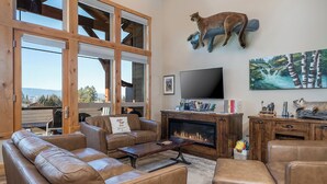 A spacious living room with leather sofas, a fireplace, a large TV, and a mounted cat statue. - 4 king beds w/ ensuites | Double the Living Space! (Bigfork)