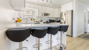 A modern kitchen with white cabinets, a stainless steel refrigerator, and a central island with black bar stools.