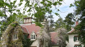 A historic building with multiple windows and a red-tiled roof, surrounded by greenery.