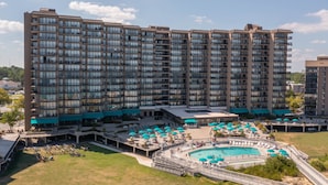 Um hotel alto com piscina na cobertura, várias varandas e um amplo espaço de estar ao ar livre com guarda-sóis.