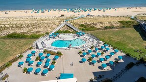 Vista aérea de um resort com piscina central, vários guarda-sóis de praia e uma extensa faixa de areia.