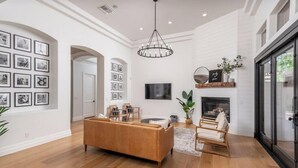 Un salon spacieux avec un plancher en bois, un canapé marron, une cheminée et une grande fenêtre.