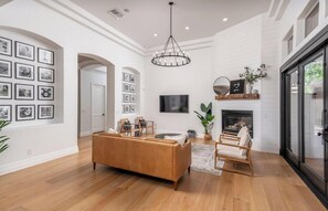 A spacious living room with a wooden floor, a brown sofa, a fireplace, and a large window.