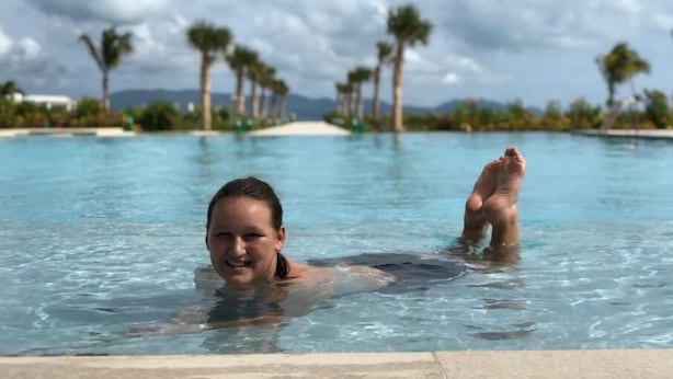 Zwembad met helder water, omringd door palmbomen en een berg in de verte.