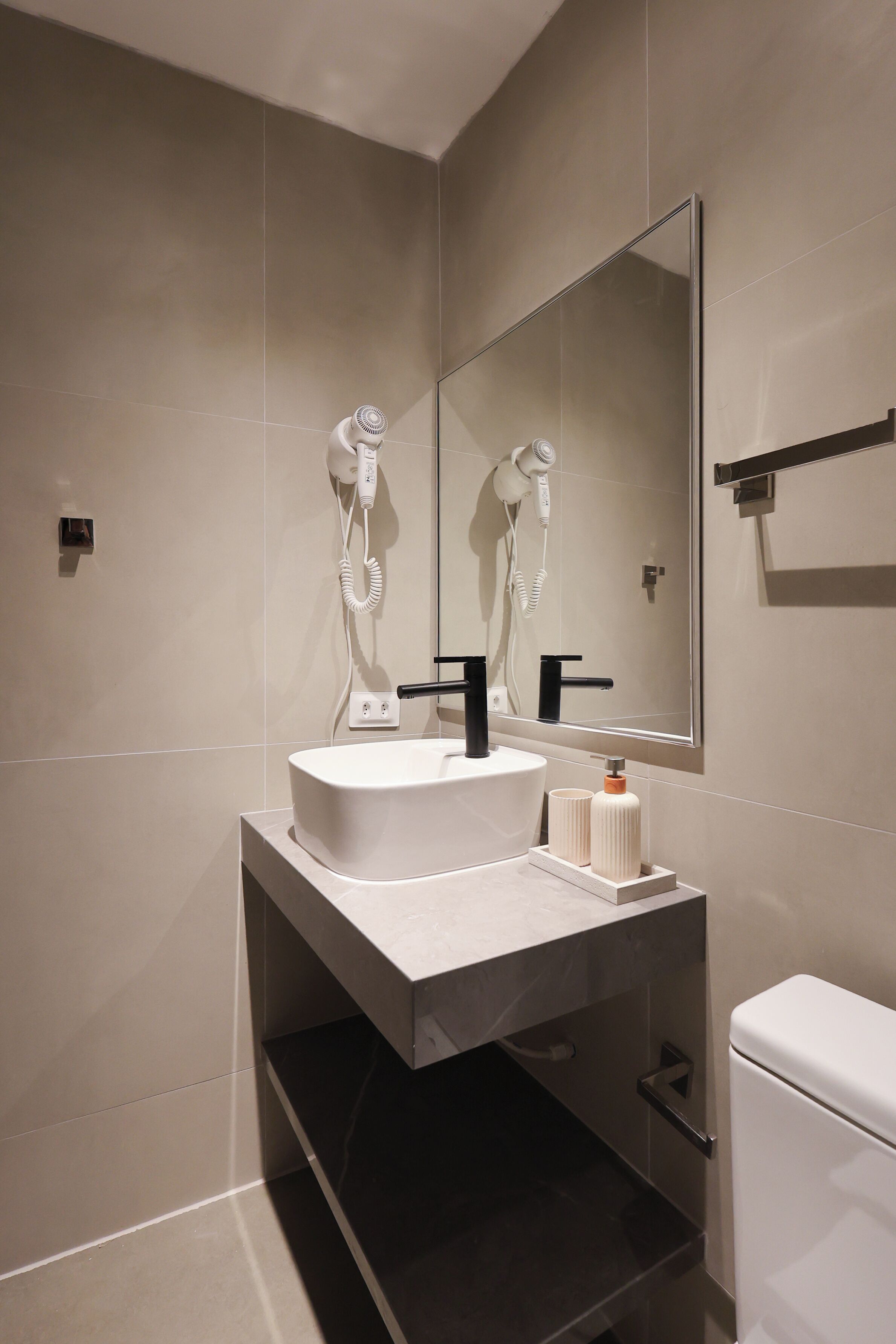 Une salle de bain moderne avec un grand miroir, un lavabo blanc et un sèche-cheveux fixé au mur.