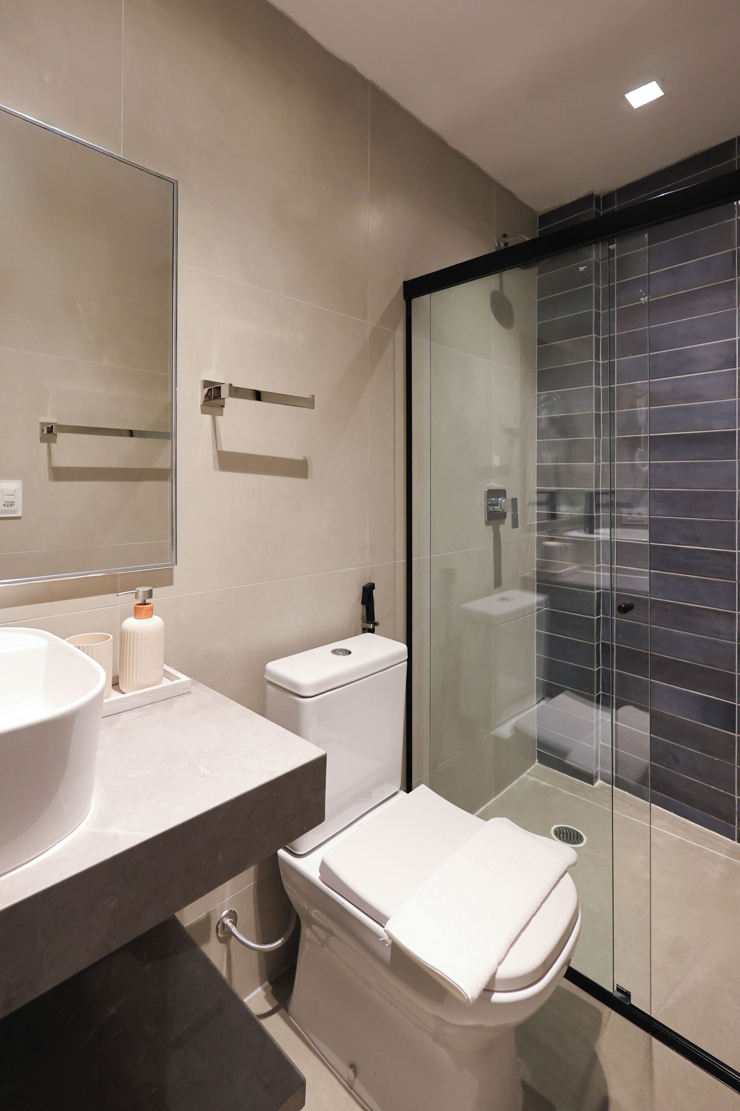 A modern bathroom with a large mirror, a white sink, a toilet, and a glass-enclosed shower area.