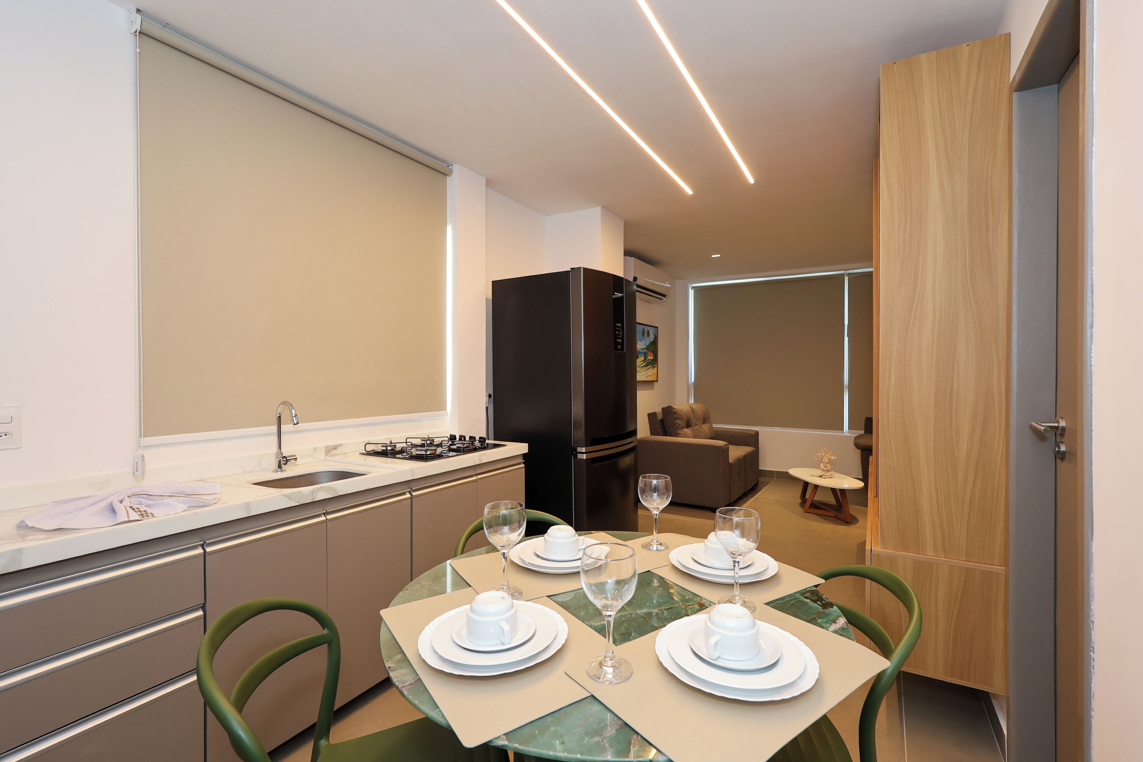 A compact kitchen with a sink, stove, and modern appliances. There is a dining area with a table set for four, chairs, and a sofa in the background.