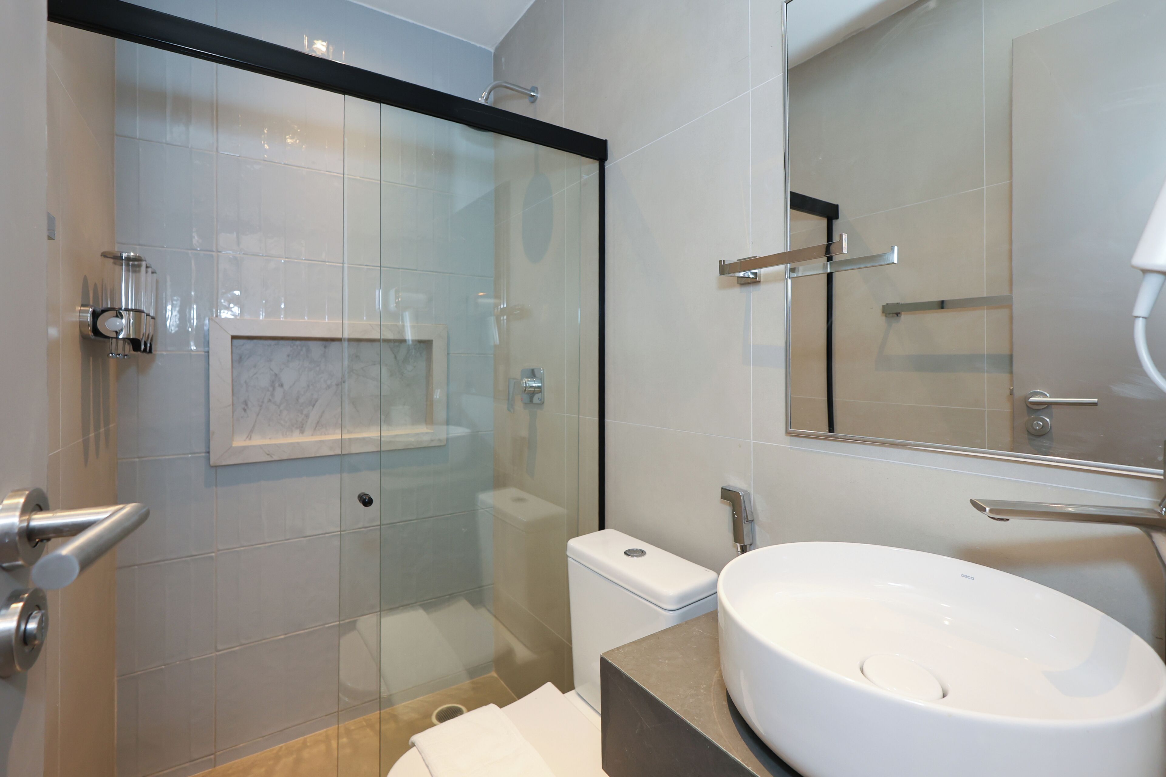 Un baño moderno con ducha envuelta en vidrio, inodoro blanco y un lavamanos grande con espejo.
