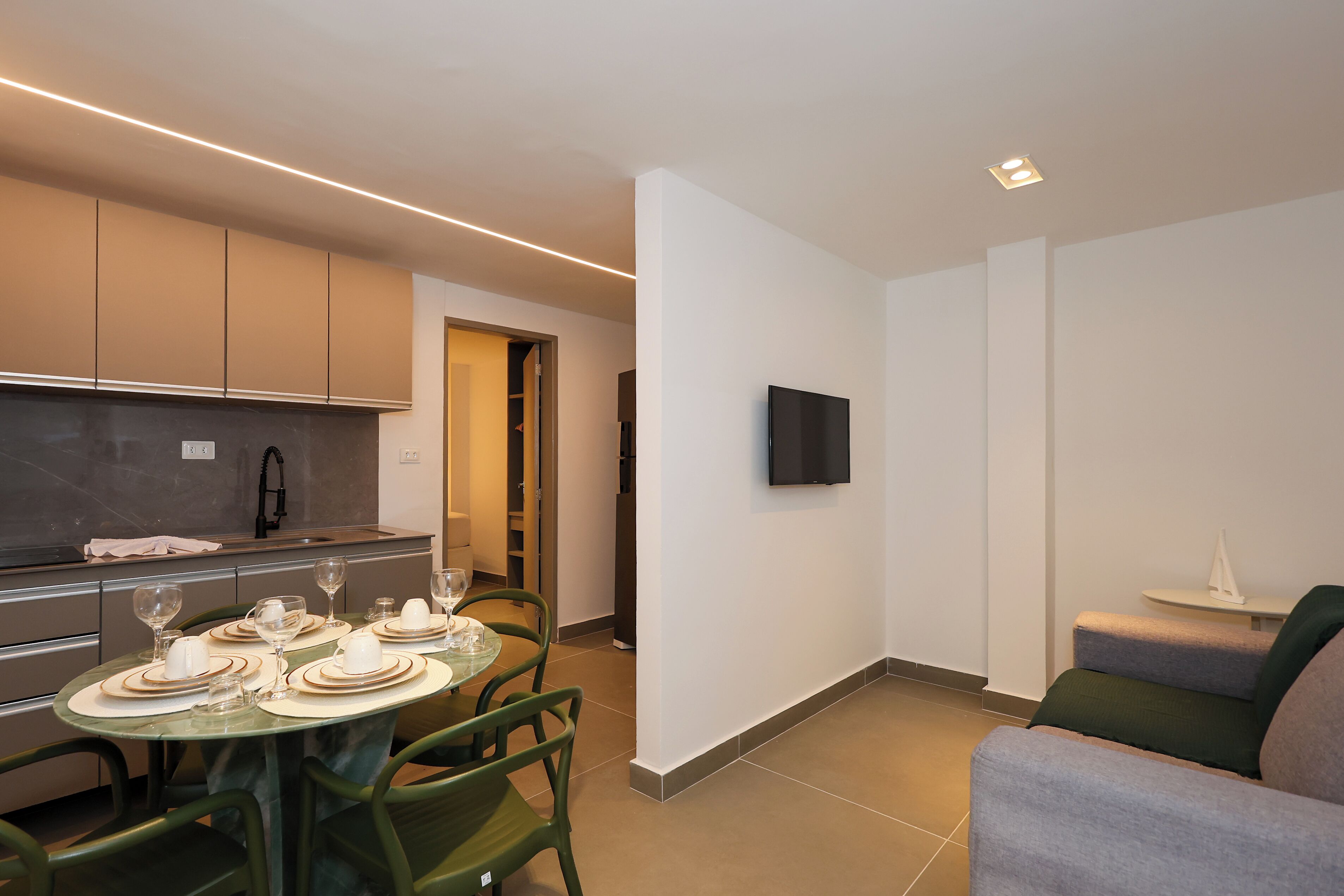 A modern living room with a dining area, a flat-screen TV mounted on the wall, and a small table with a ship model.