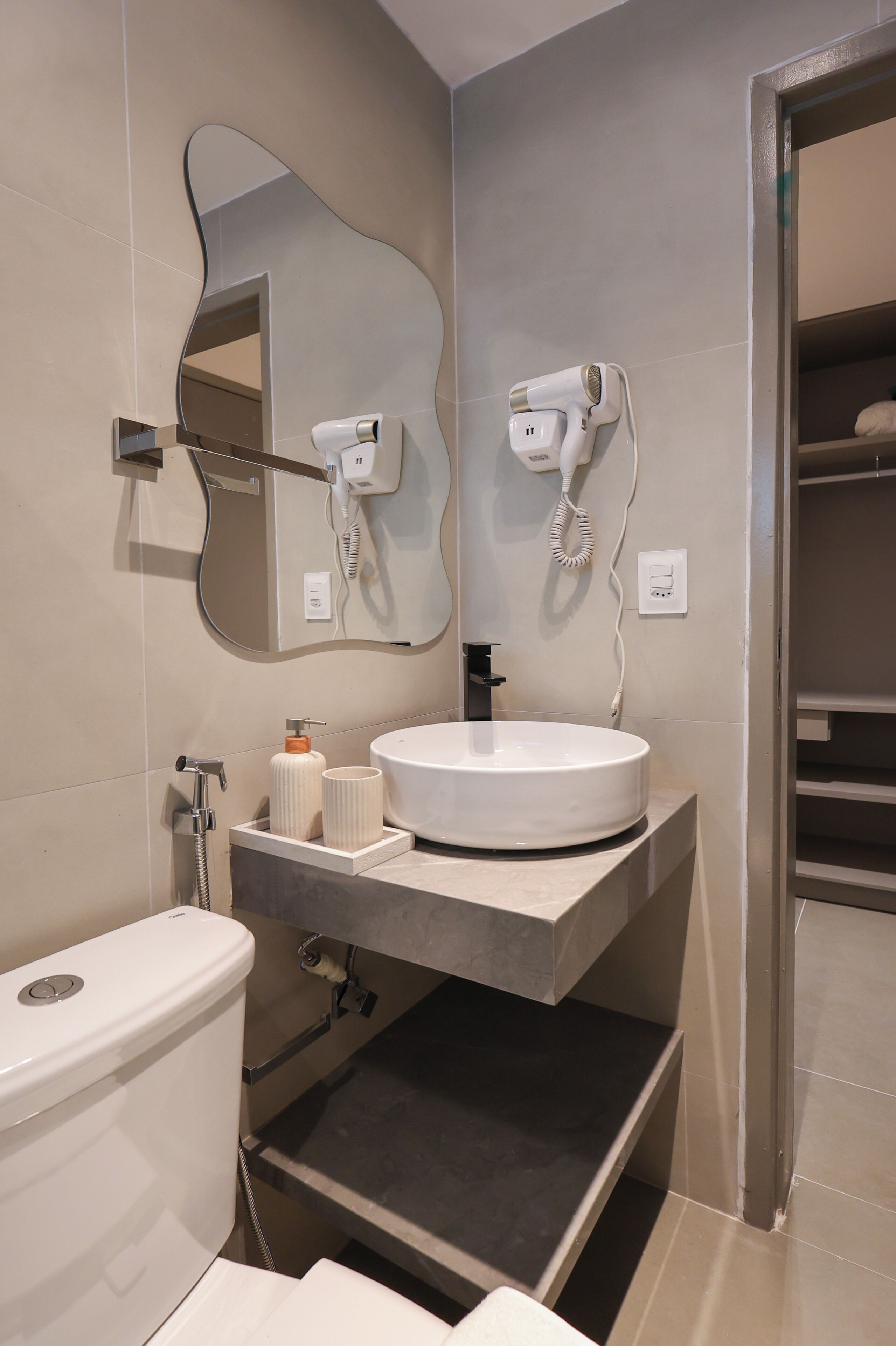 Ein modernes Badezimmer mit einem runden Waschbecken, einer Toilette, einem Fön und einem Spiegel.