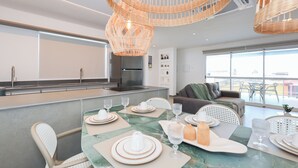 Une cuisine moderne dotée d’un réfrigérateur encastré, d’un coin repas avec une table en marbre pouvant accueillir quatre personnes, et d’une grande fenêtre offrant une vue sur l’extérieur.