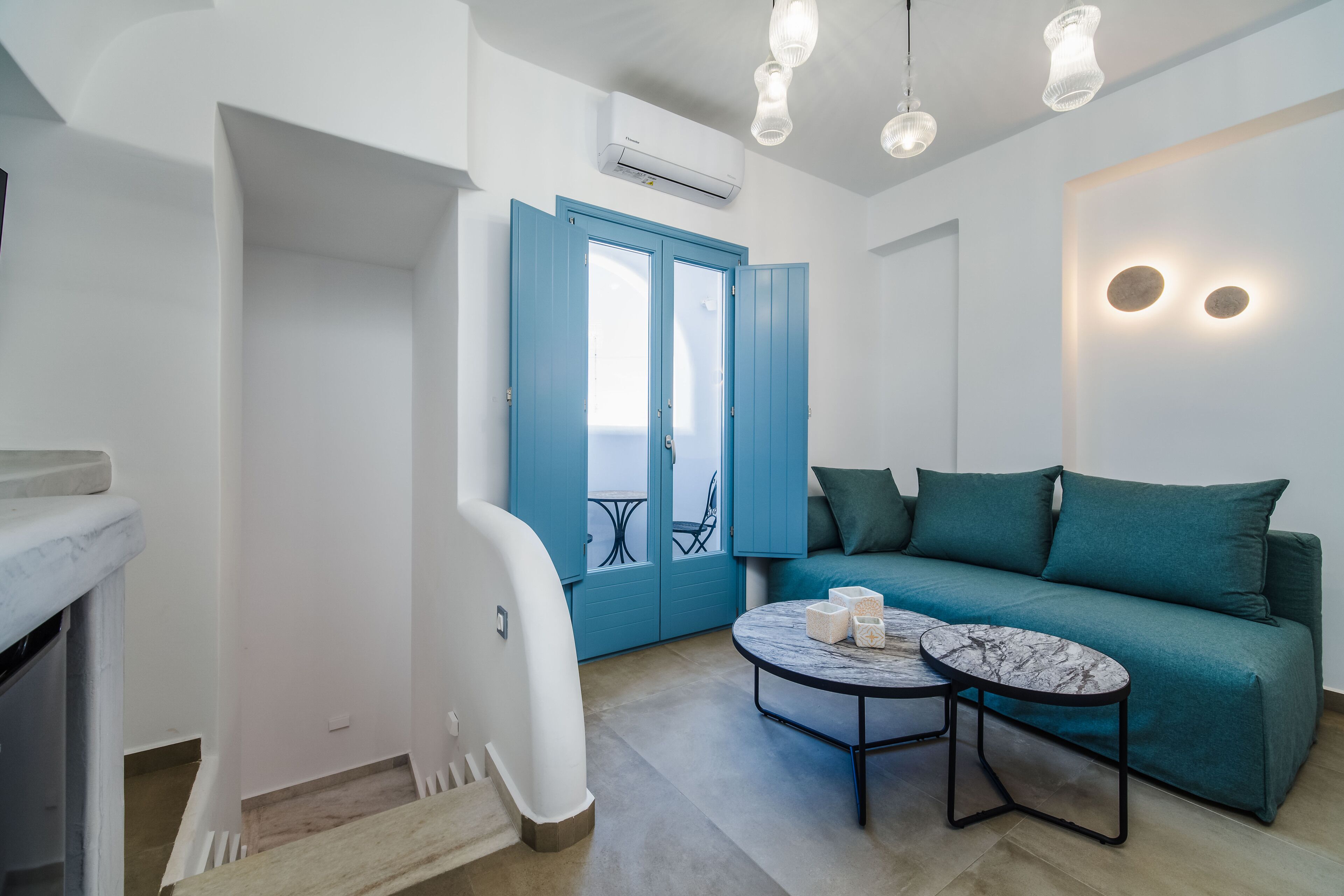 A modern living room with a teal sofa, a round coffee table, and a blue door leading to a balcony.