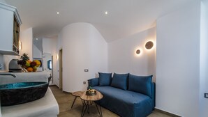 A modern living room with a blue sofa, a round wooden table, and a bowl of fruit. - Aegean Blue Luxury Suites (Santorini)
