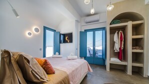 A bedroom with a bed, a wardrobe, a TV, and a view of the outside. - Aegean Blue Luxury Suites (Santorini)