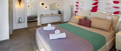 A modern bedroom with a large bed, a bedside table, a desk, and a mirror.