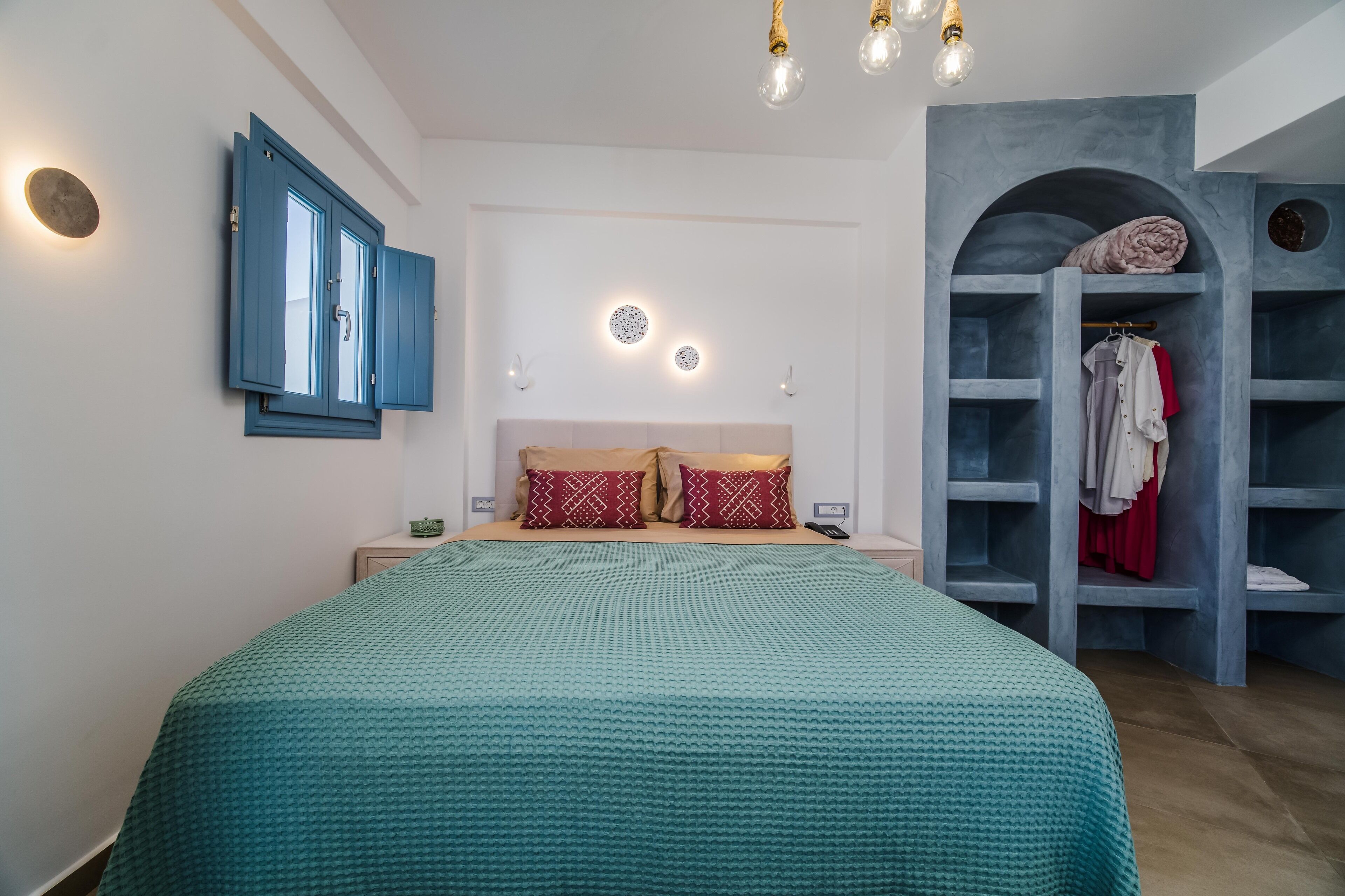 A bedroom with a bed, a wardrobe, and a built-in shelf with clothes.