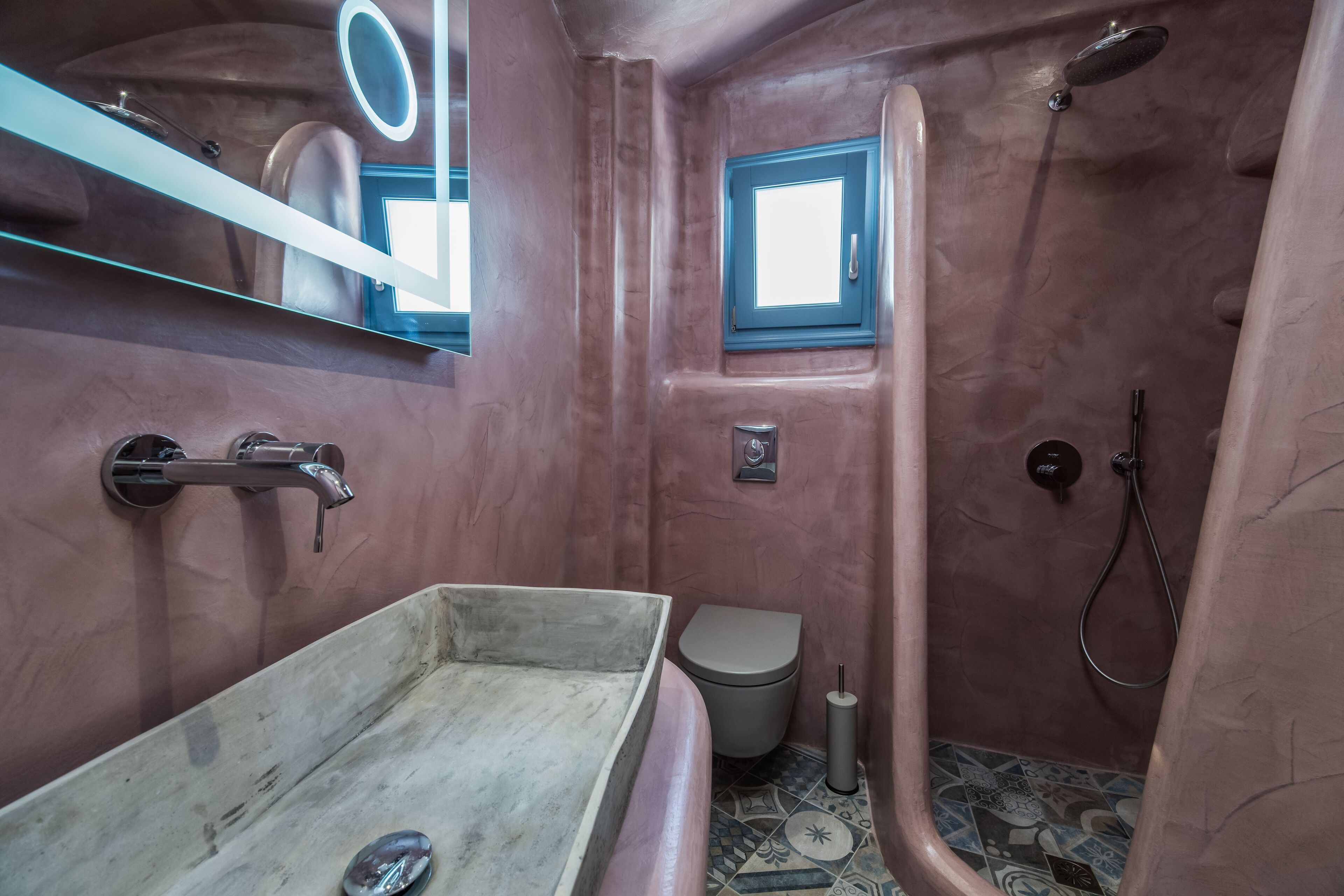 Un baño con un lavamanos rectangular, un inodoro, una ducha y un espejo con marco redondo.