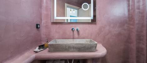 Een badkamer met een roze wand, een rechthoekige spiegel met verlichting, een rechthoekig wastafelmeubel en een handdoekhouder.