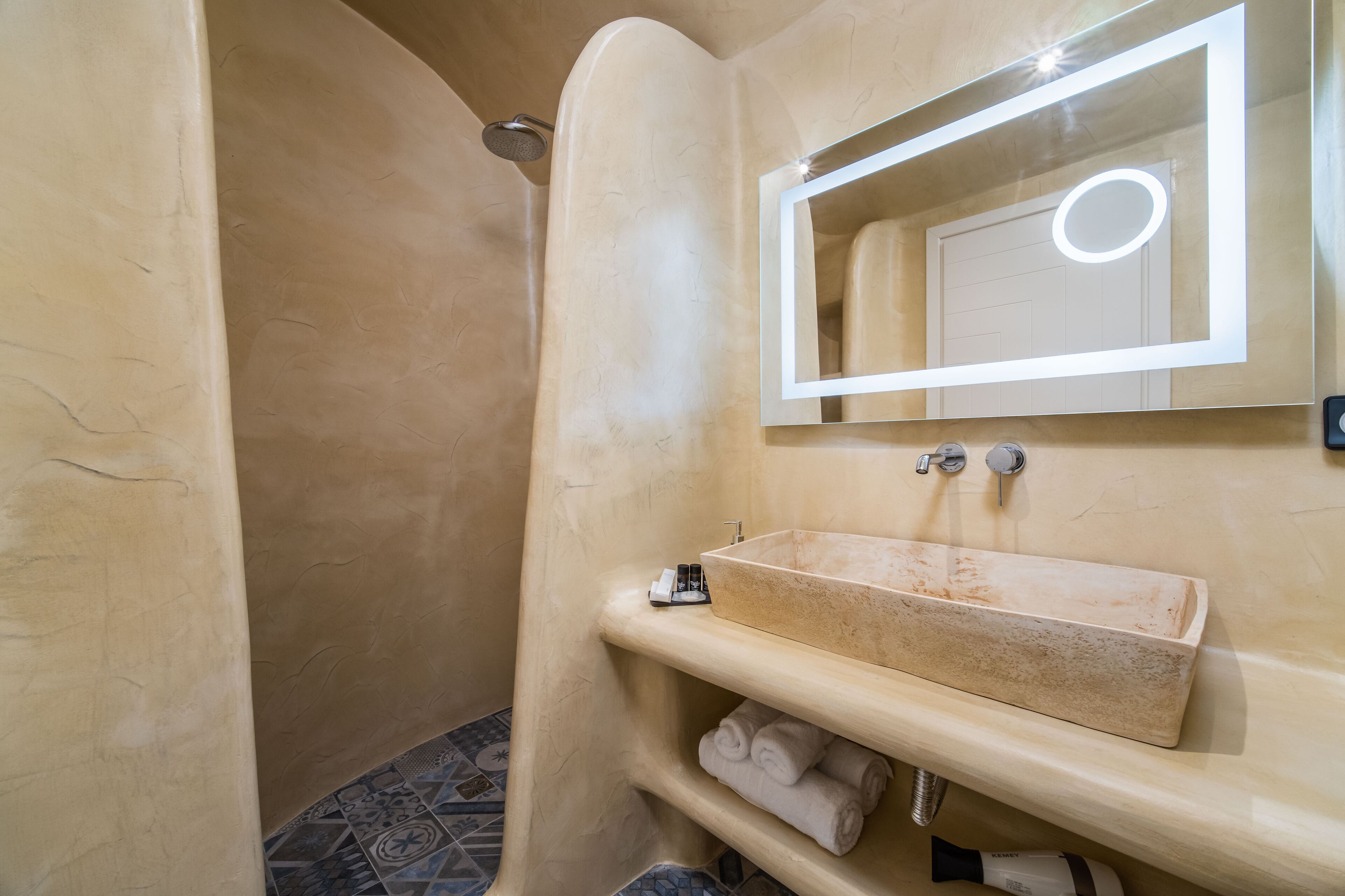 Een badkamer met een beige wastafel, een spiegel met verlichting en een douche.