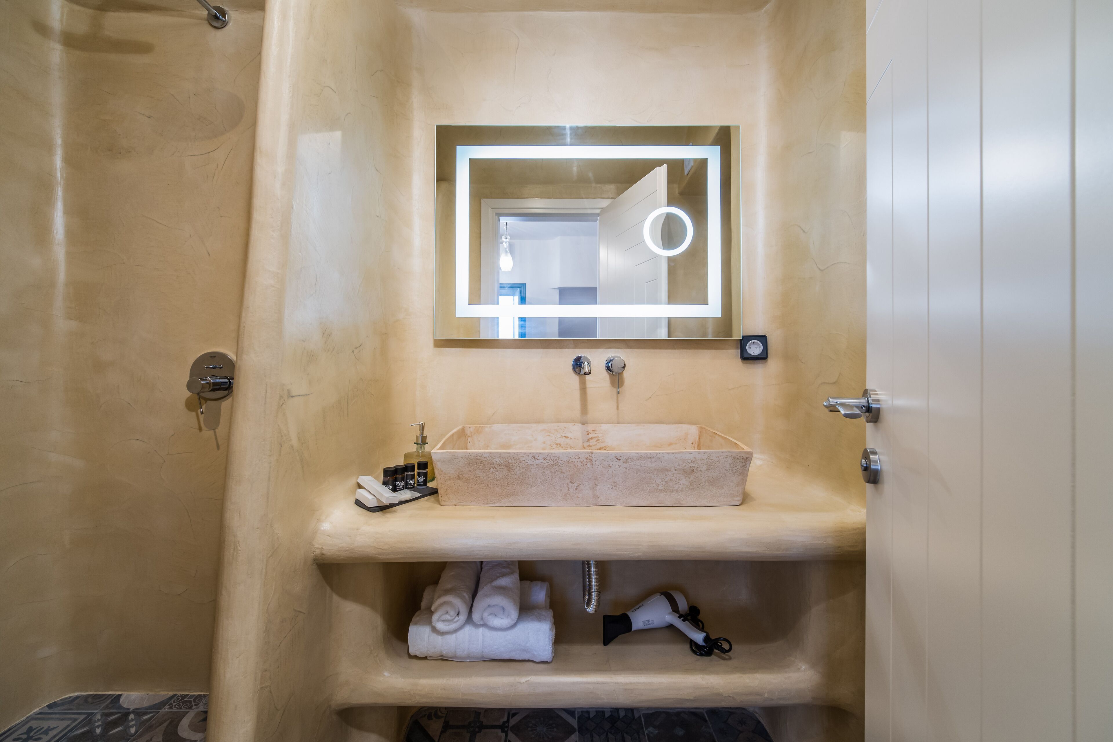 A bathroom with a beige sink, a mirror with a light, and a towel rack.