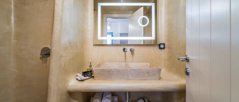A bathroom with a beige sink, a mirror with a light, and a towel rack.