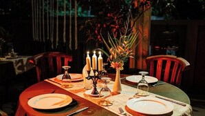 A dining table set for four with candles, a vase with flowers, and a candle holder.