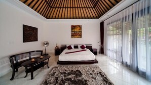 A spacious bedroom with a large bed, a bench, a fan, and artwork on the walls. - Rossa Garden Hotel (Karangasem)