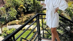 A person in a white robe standing on a balcony with a view of a tropical landscape. - Rossa Garden Hotel (Karangasem)