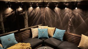 A cozy seating area with a cushioned bench and a small table, featuring a lantern and a patterned throw blanket.