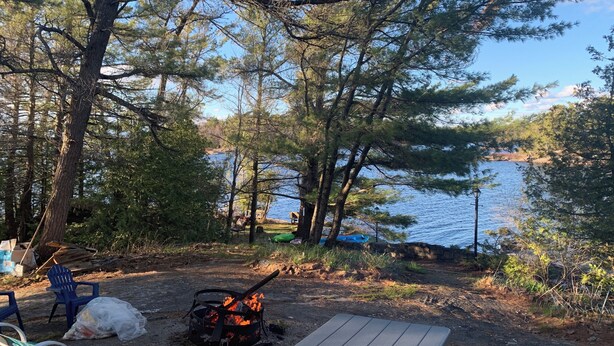 A campsite with a fire pit, chairs, and a view of a lake.