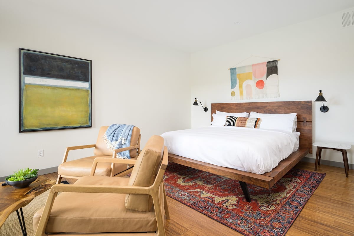 A bedroom with a bed, a chair, a rug, and a painting on the wall.